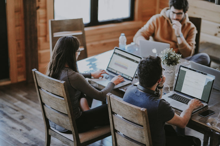 three employees sitting around a table laughing on their laptops seeing the benefit of allowing employee CBD use at work